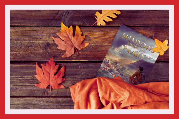 Shadows Among the Peaks by R.D. Smithson beside autumn leaves and an orange blanket.