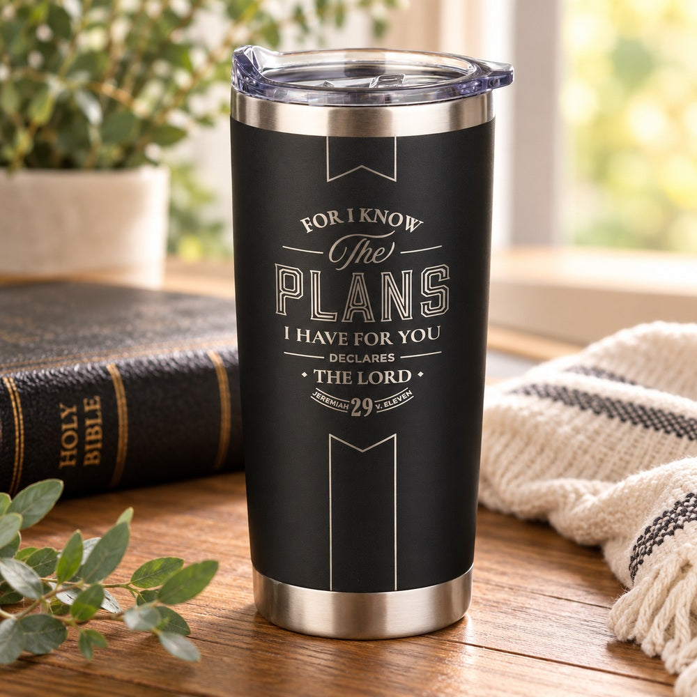 Black I Know the Plans Jeremiah 29:11 stainless steel tumbler on a wooden table beside a Bible in a warmly lit setting.