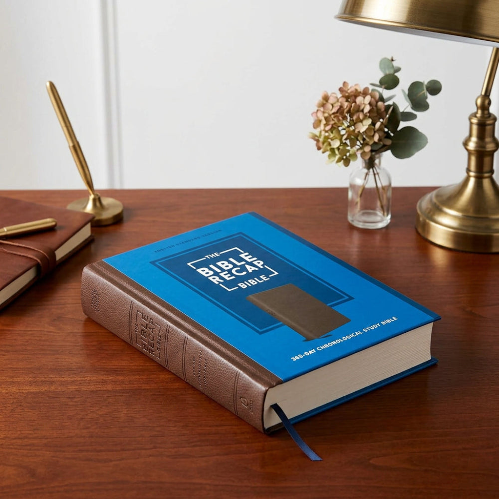 The Bible Recap Bible on a wooden desk beside a lamp and flowers.
