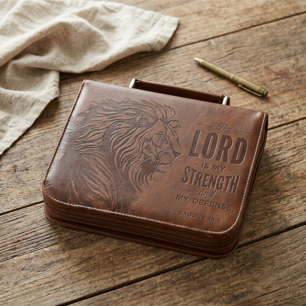 The Lord Is My Strength honey-brown lion Bible cover on a wooden table beside a pen