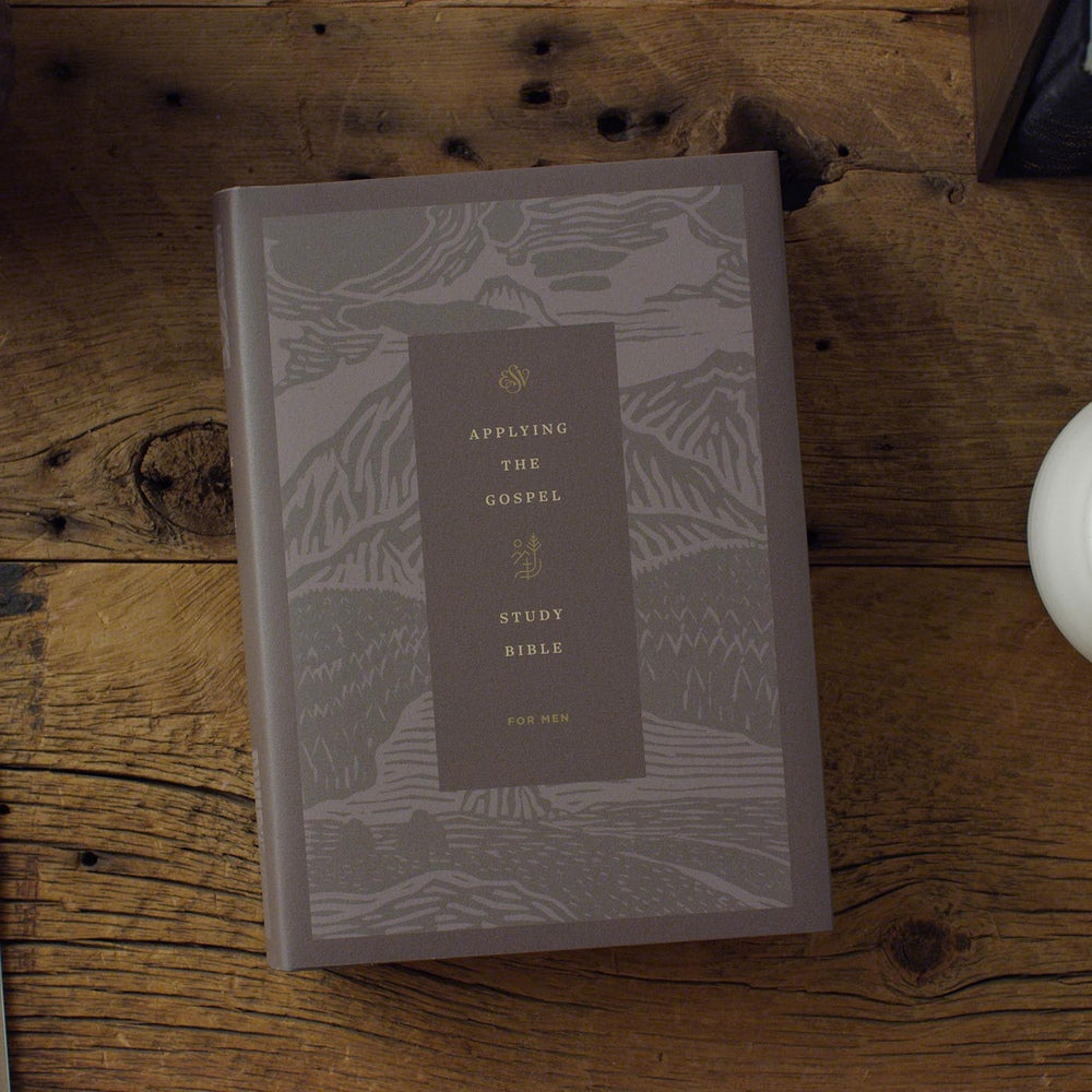 Gray forest-pattern hardcover ESV Applying the Gospel Study Bible for Men resting on a wooden table.