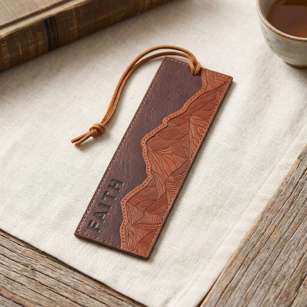 Faith Can Move Mountains brown faux leather bookmark on light fabric, with a cord and mountain design