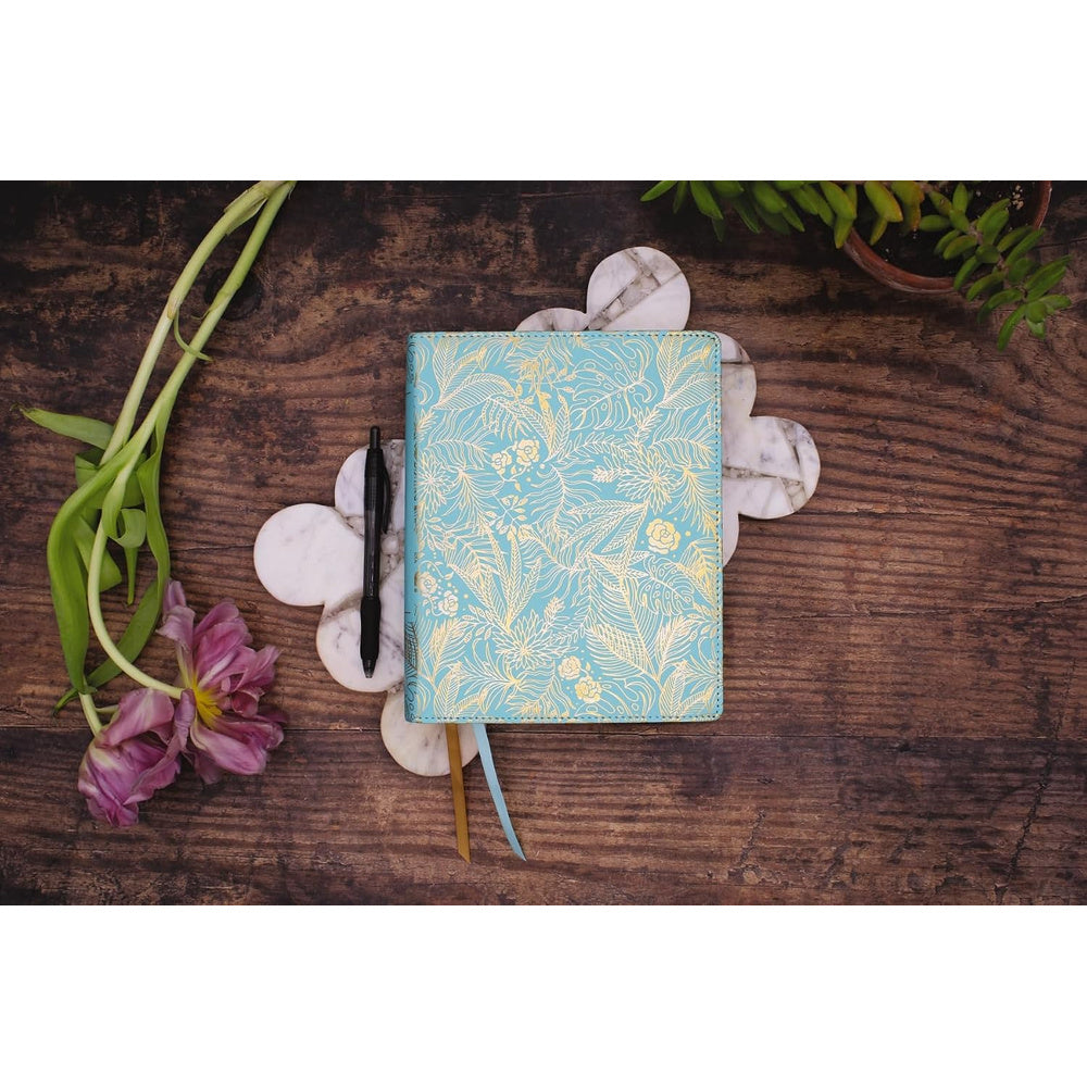 Teal NIV Journal the Word Bible for Women resting on a wooden table with flowers and ribbon markers.