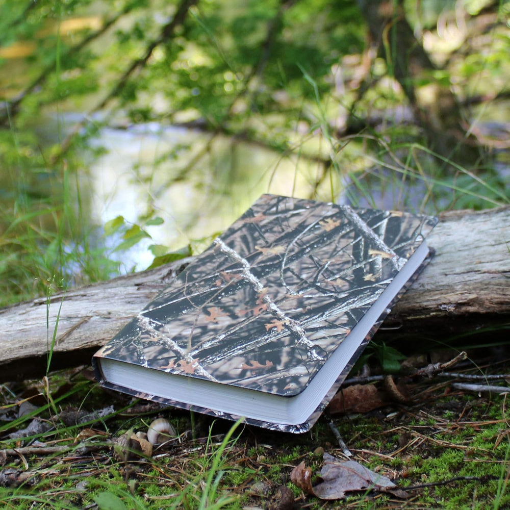 Lost Camo NIV Outdoorsman Bible resting closed on a log outdoors.