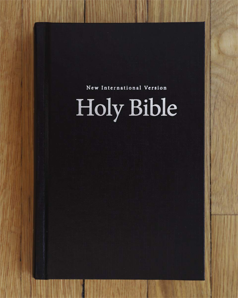 Black front cover of the NIV Value Pew and Worship Bible on a wooden surface.